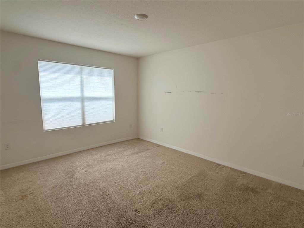 An empty bedroom features beige carpet, off-white walls, and a window with pleated shades — 2916 SUNRIDGE LOOP, ST CLOUD, FL
