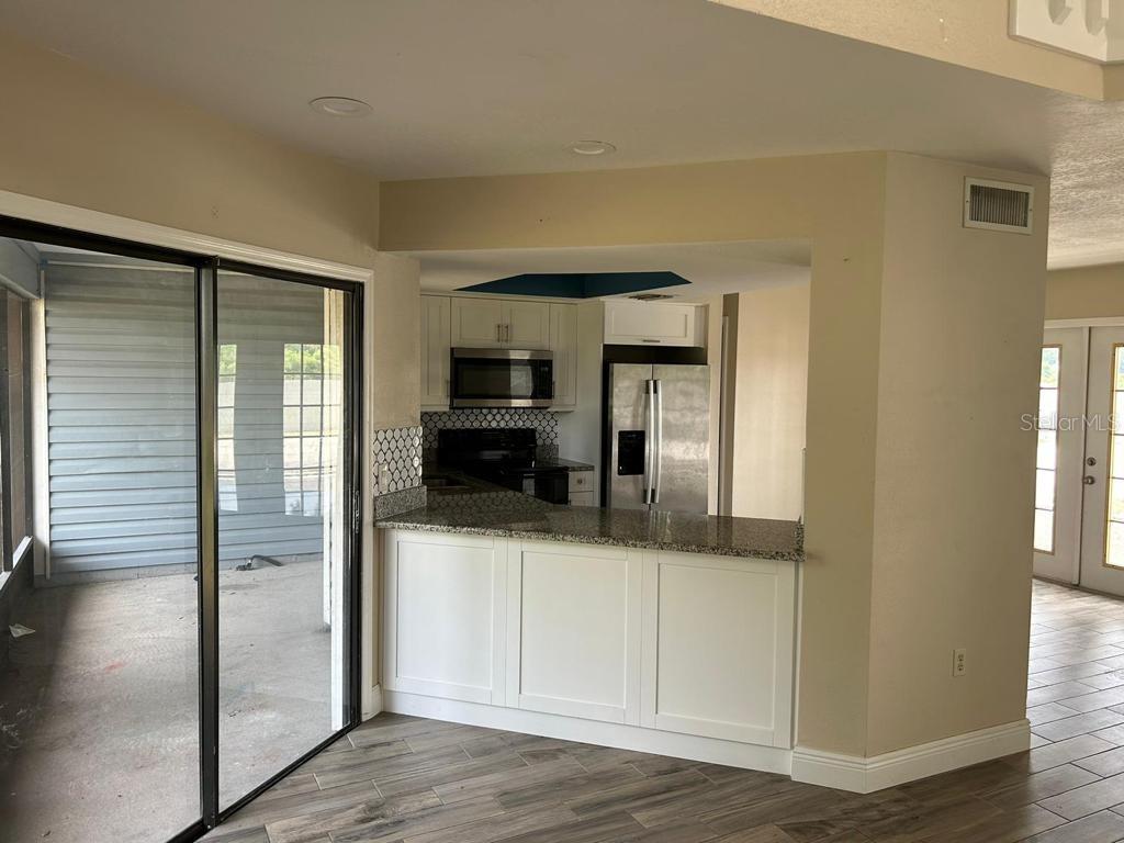 A kitchen with white cabinets and granite countertops overlooks a tiled patio through sliding doors — 222 CARPENTERS WAY UNIT 6, LAKELAND, FL