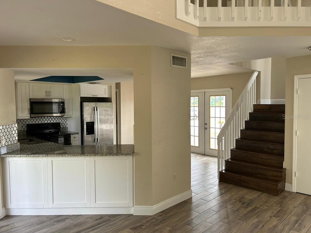 A kitchen with white cabinets and granite countertops overlooks a living area with stairs — 222 CARPENTERS WAY UNIT 6, LAKELAND, FL