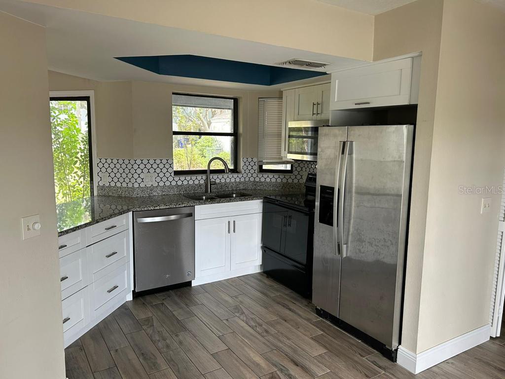 A kitchen features white cabinets, stainless steel appliances, granite countertops, and wood-look tile flooring — 222 CARPENTERS WAY UNIT 6, LAKELAND, FL