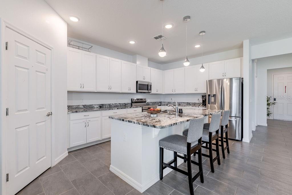 A kitchen features white cabinets, granite countertops, a center island with bar stools, and tile flooring — 3319 CURLEW AVENUE, LEESBURG, FL