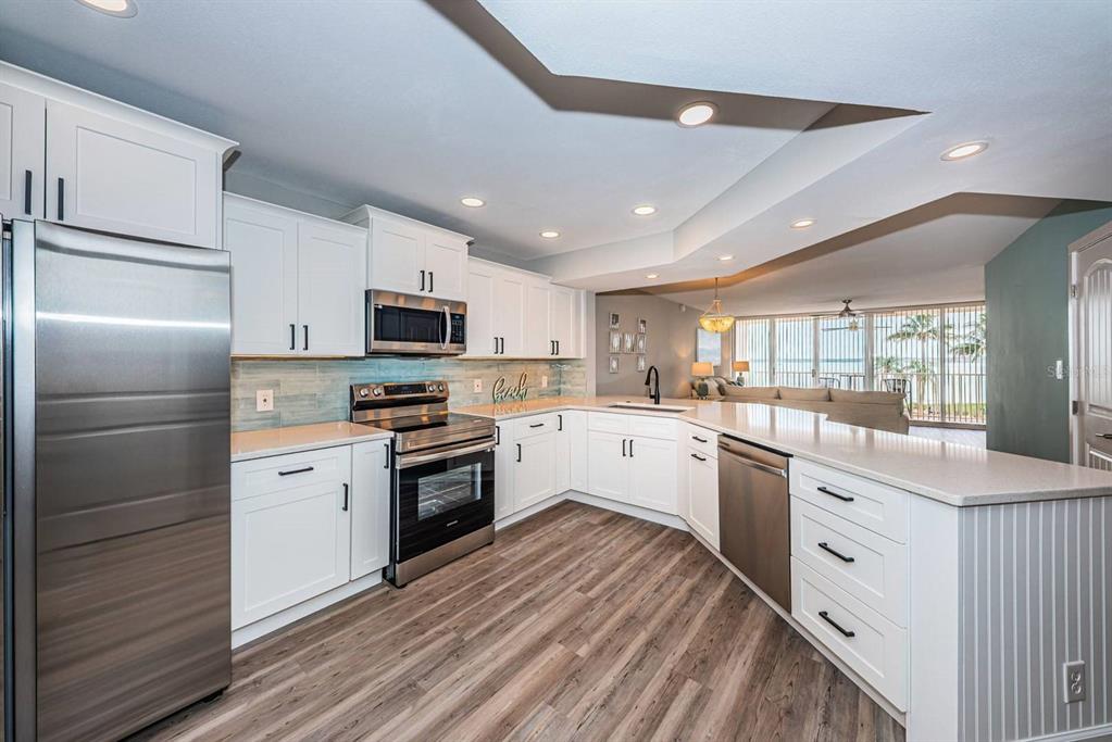 A modern kitchen features white cabinets, stainless steel appliances, and a peninsula overlooking a living area — 5151 ISLA KEY BOULEVARD S UNIT 220, ST PETERSBURG, FL