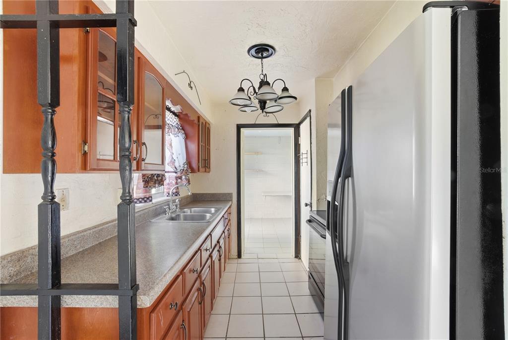 A narrow galley kitchen features wood cabinets, a stainless steel refrigerator, and white tile flooring — 800 ORANGE GROVE DRIVE, ALTAMONTE SPRINGS, FL