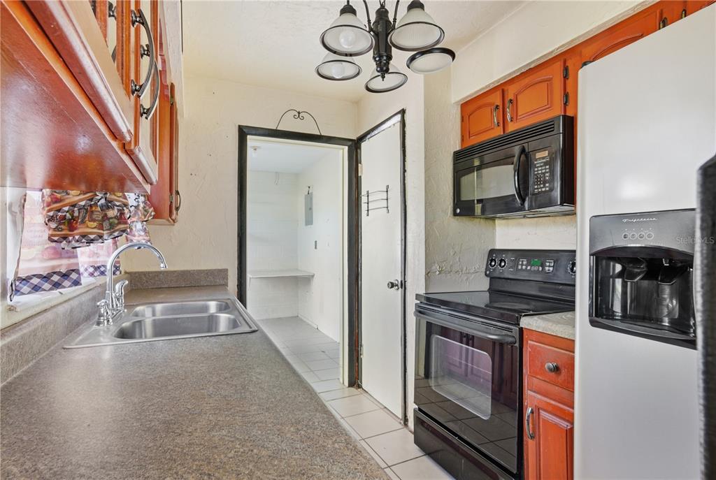 A kitchen features wood cabinets, black appliances, a double sink, and a doorway to utility — 800 ORANGE GROVE DRIVE, ALTAMONTE SPRINGS, FL