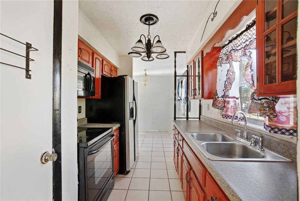 A galley kitchen features orange cabinets, black appliances, a double sink, and tiled flooring — 800 ORANGE GROVE DRIVE, ALTAMONTE SPRINGS, FL