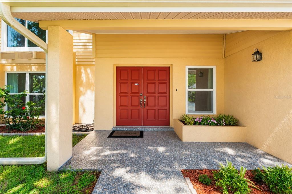 A front porch with a red double door, a window, and a raised planter bed — 10904 AUTUMN OAK PLACE, TAMPA, FL