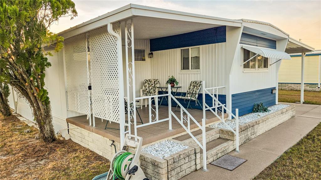 A mobile home features a covered front porch with white lattice, railings, and outdoor seating — 5227 BETTY STREET, ZEPHYRHILLS, FL