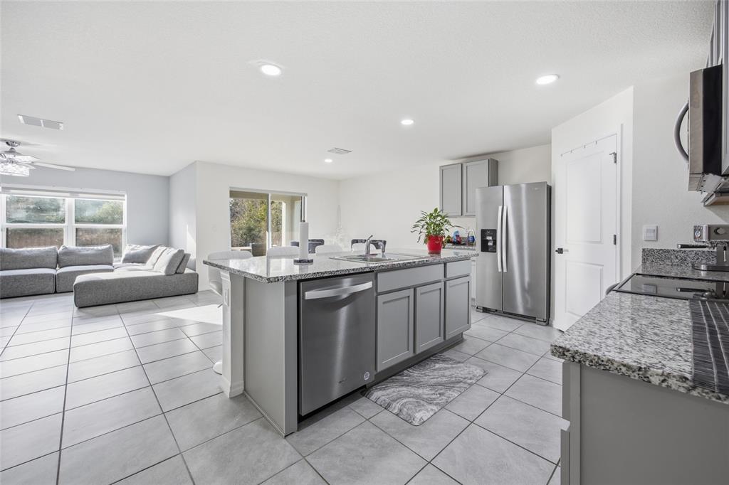A kitchen with a granite-topped island, stainless steel appliances, and gray cabinets, opening to a living area — 16402 SW 17TH TERRACE ROAD, OCALA, FL