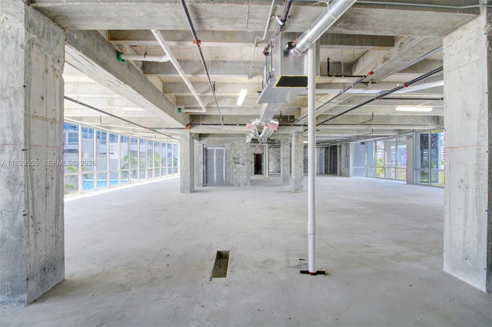 An unfinished commercial interior features exposed concrete ceilings, support columns, and large floor-to-ceiling windows — 6930 Collins Ave # O1, Miami Beach FL 33141, MIAMI BEACH, FL