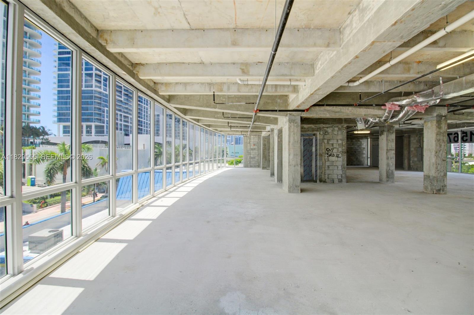 An unfinished commercial space features concrete floors, exposed ceiling pipes, and floor-to-ceiling windows — 6930 Collins Ave # O1, Miami Beach FL 33141, MIAMI BEACH, FL