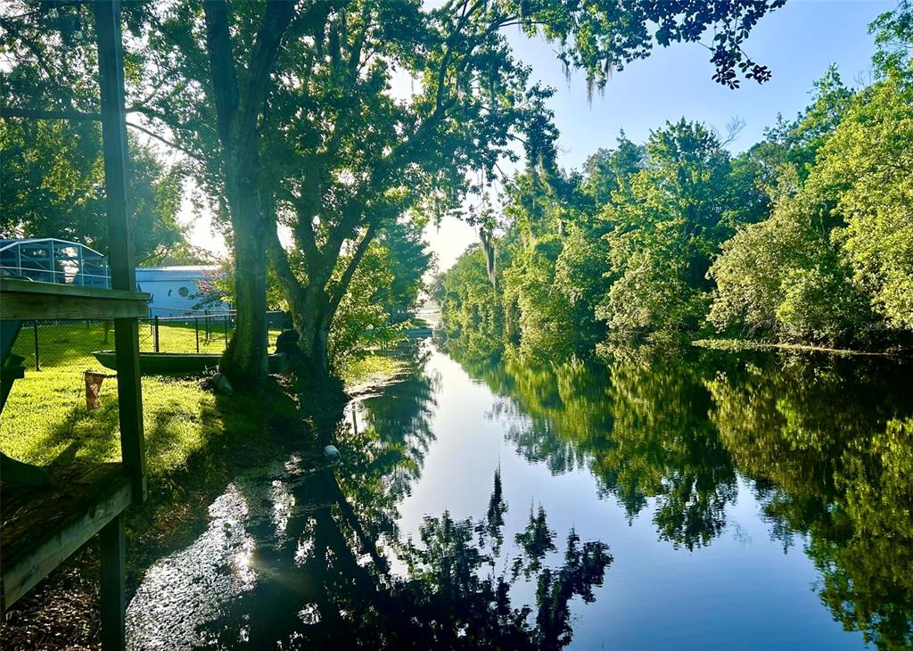 A view of a narrow canal lined with lush green trees and a grassy bank — 6590 BAY SHORE DRIVE, ST CLOUD, FL