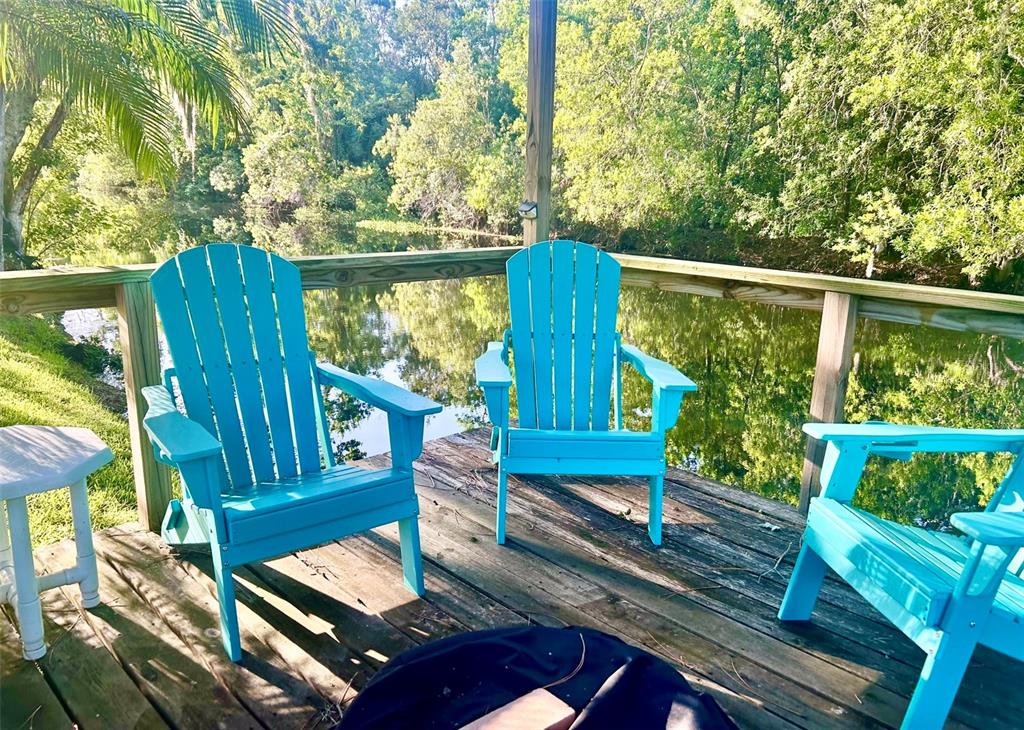 Three bright blue Adirondack chairs sit on a wooden deck overlooking a calm pond — 6590 BAY SHORE DRIVE, ST CLOUD, FL