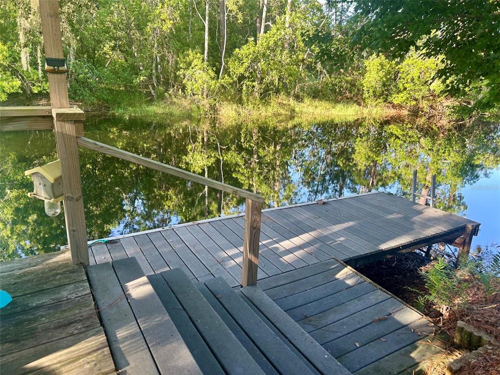 A wooden deck with stairs leads to a dock overlooking a calm, tree-lined pond — 6590 BAY SHORE DRIVE, ST CLOUD, FL