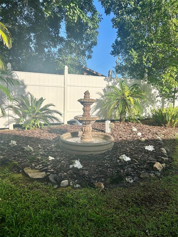 A tiered stone fountain sits in a mulched garden bed in front of a white fence — 6590 BAY SHORE DRIVE, ST CLOUD, FL