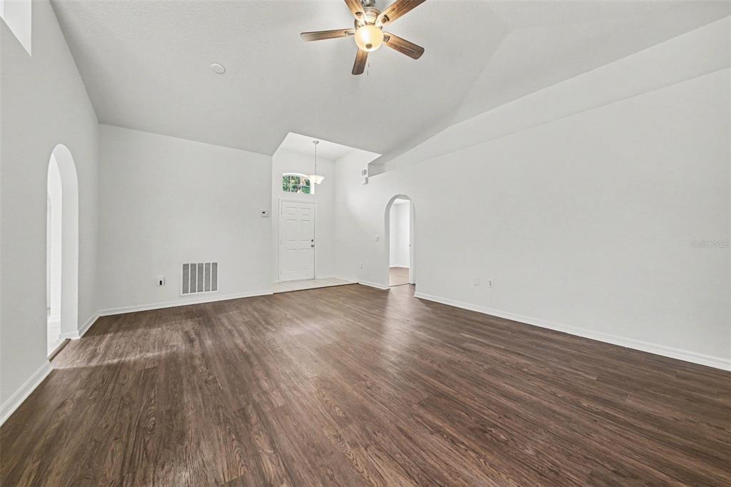 An empty living room features white walls, vaulted ceilings, and dark wood-look flooring — 332 MCKAY BOULEVARD, SANFORD, FL