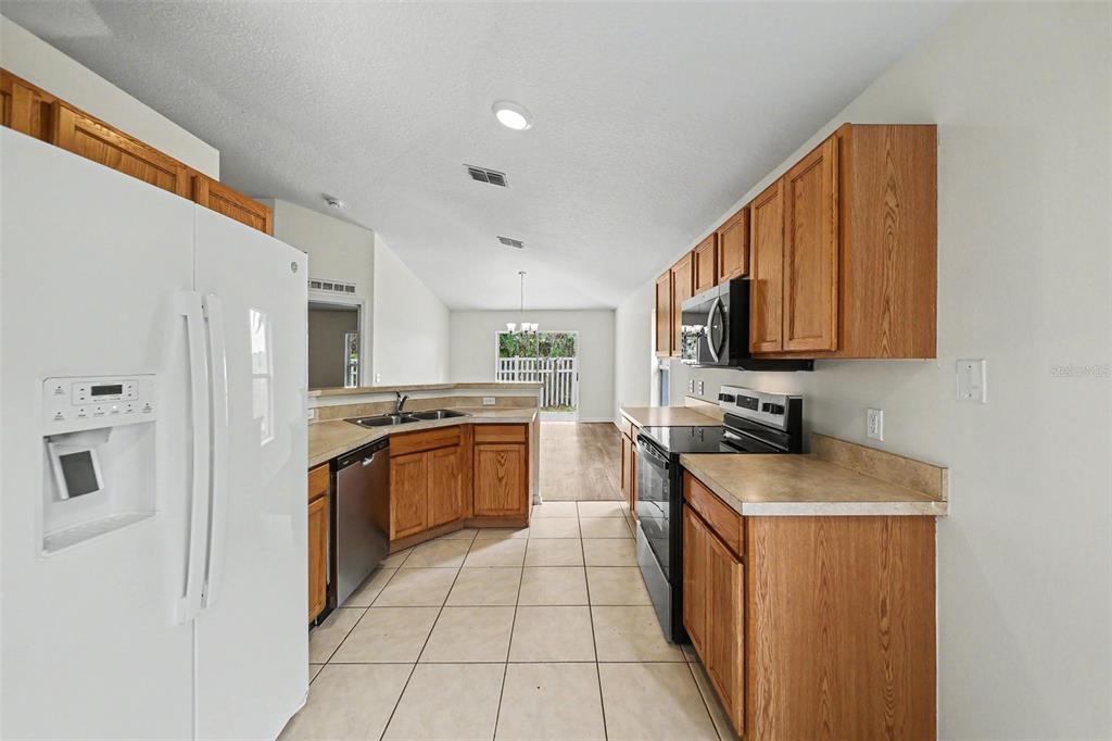 A kitchen with wood cabinets, white appliances, and tile flooring leads to a dining area — 332 MCKAY BOULEVARD, SANFORD, FL