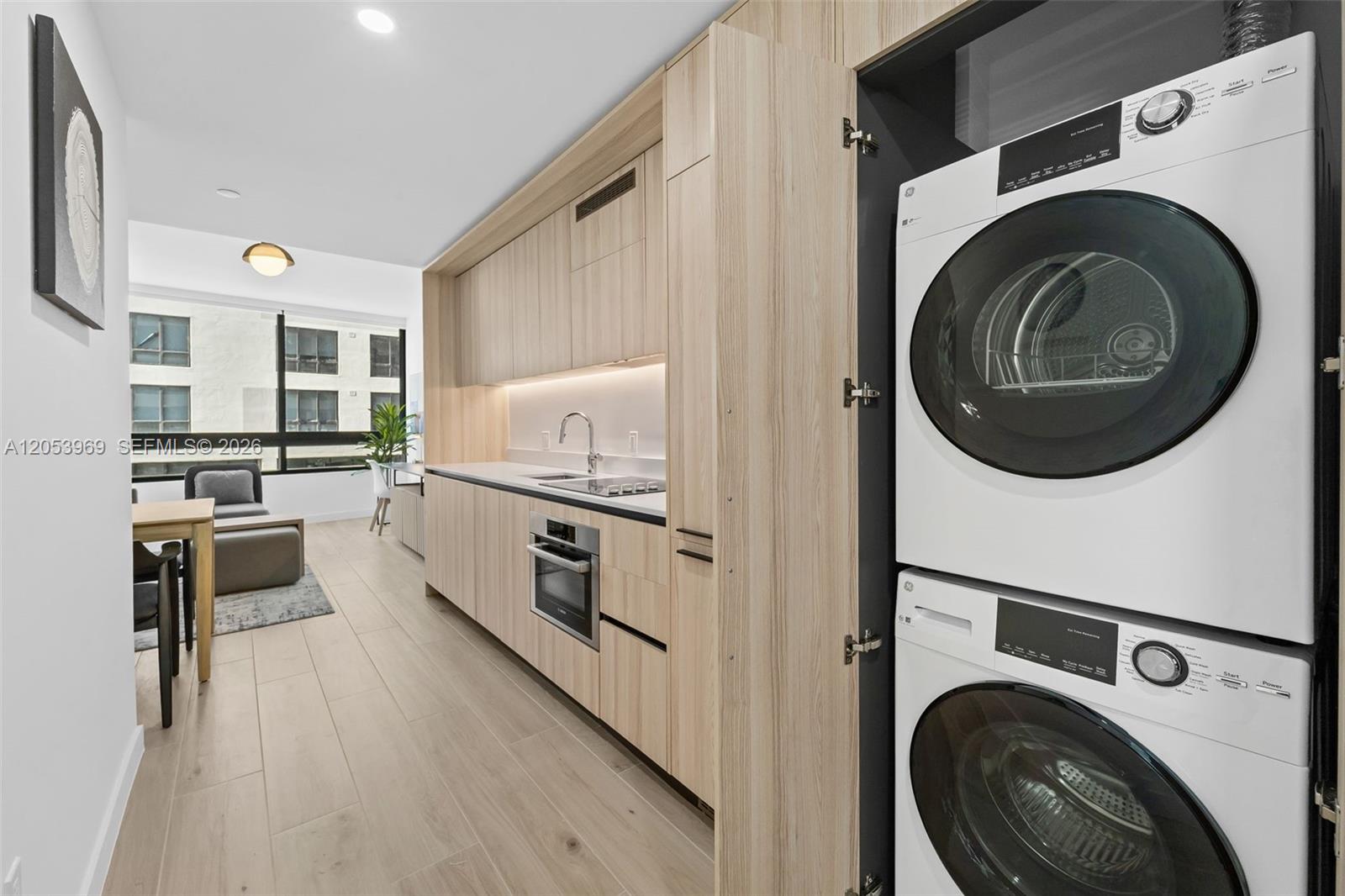 A modern kitchen features light wood cabinetry, built-in appliances, and a stacked washer-dryer unit — 225 N Miami Ave # 912, Miami FL 33128, MIAMI, FL
