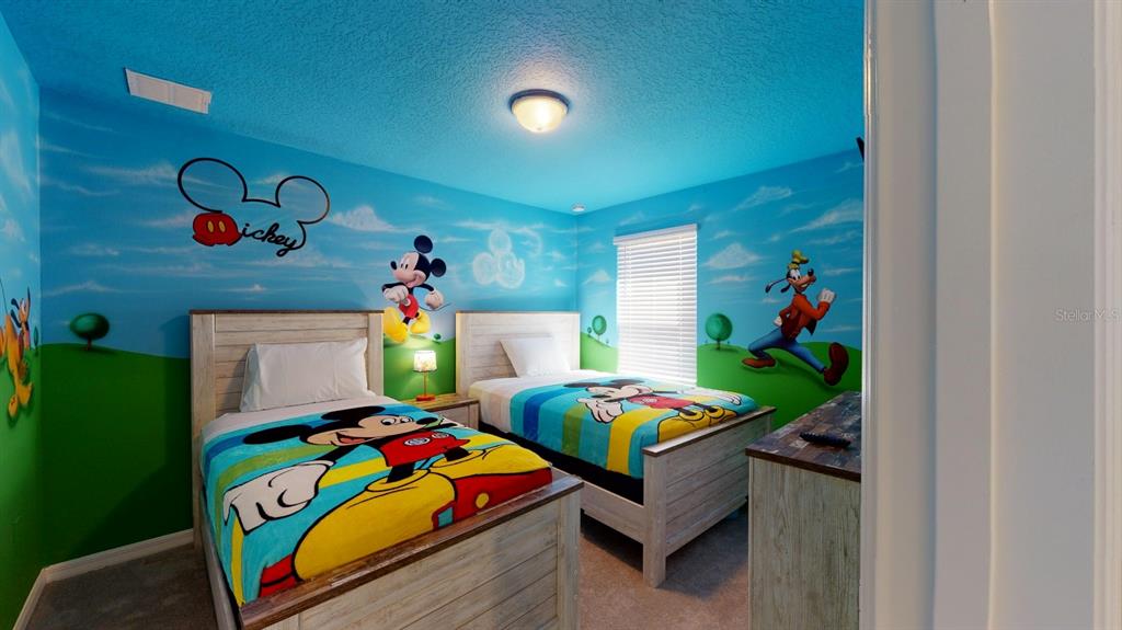 A bedroom with two twin beds features Disney-themed wall murals and light-colored wooden furniture — 2438 TANGER DRIVE, KISSIMMEE, FL