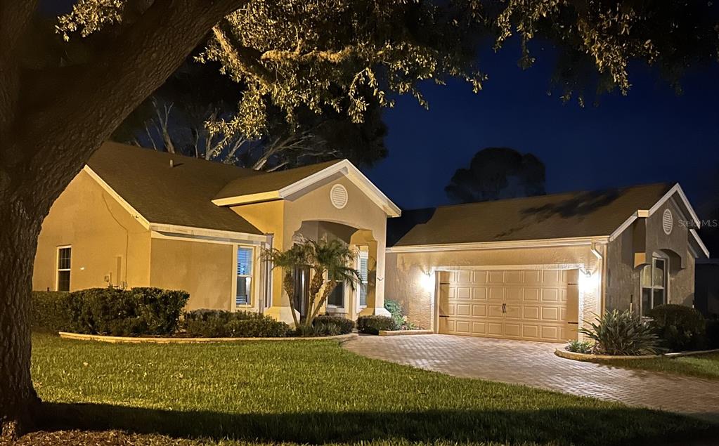 A single-story house with a paved driveway and a two-car garage at night — 7029 PINE HOLLOW DRIVE, MOUNT DORA, FL
