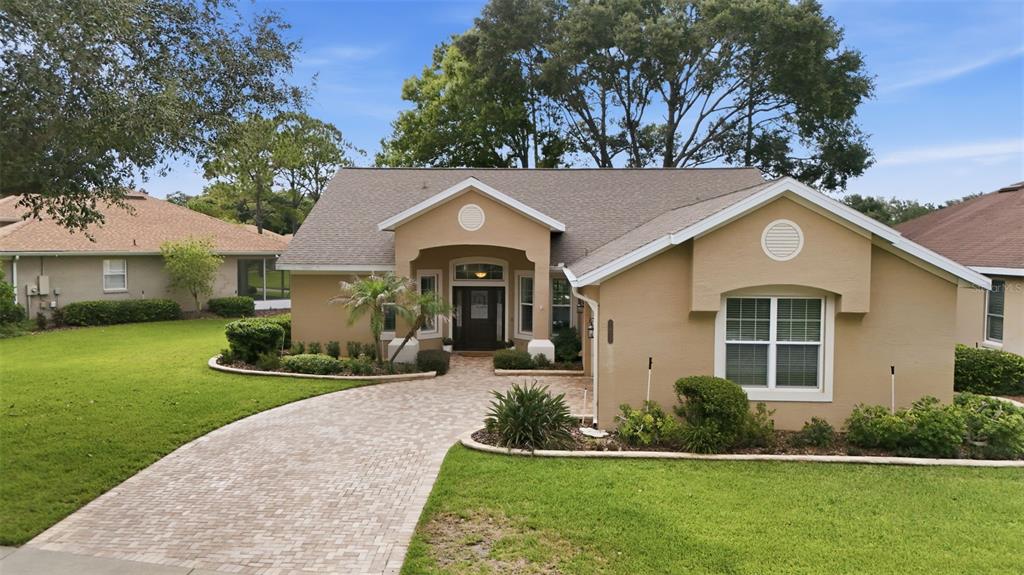 A single-story tan house with a paved driveway and a landscaped front yard — 7029 PINE HOLLOW DRIVE, MOUNT DORA, FL