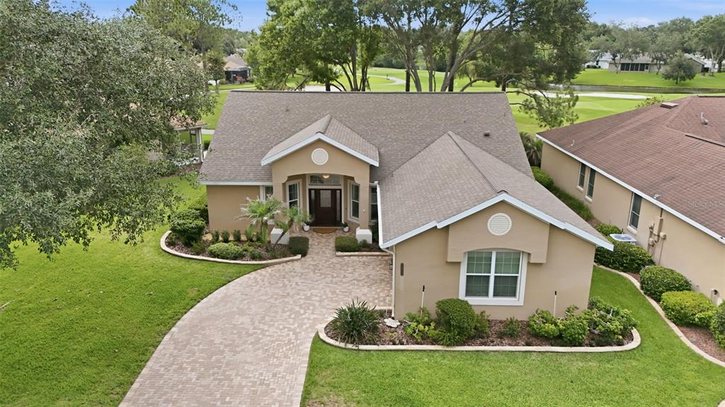 An aerial view shows a tan, single-story house with a paved driveway and a golf course — 7029 PINE HOLLOW DRIVE, MOUNT DORA, FL