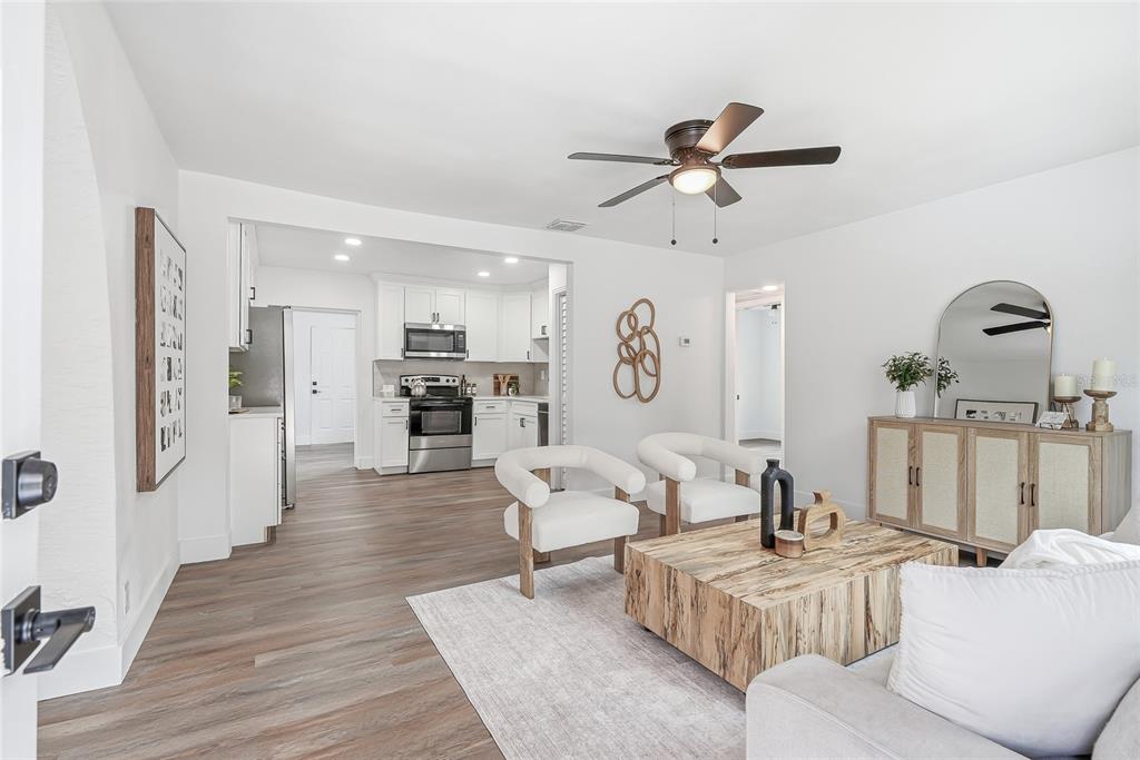 A living room with wood-look flooring opens into a white kitchen with stainless steel appliances — 2534 19TH STREET S, ST PETERSBURG, FL