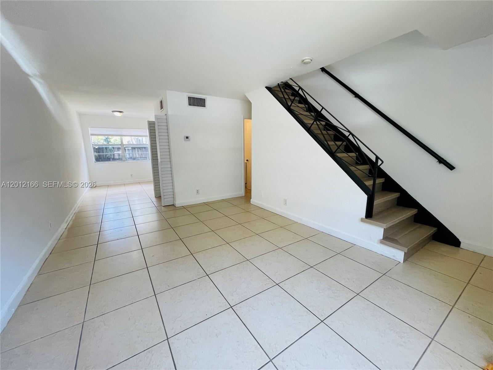 An empty room with light-colored tile flooring and a black-railed staircase leading upstairs — 825 NW 46th Ave # 825, Plantation FL 33317, PLANTATION, FL
