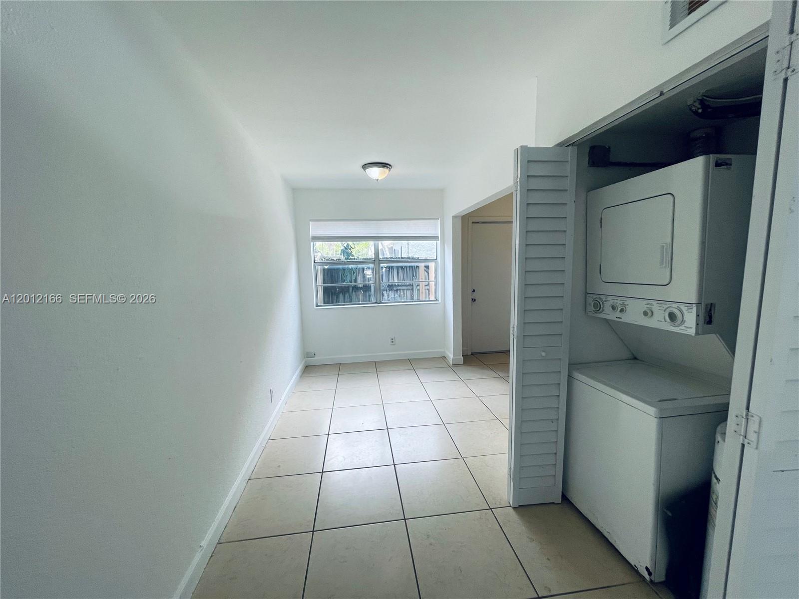 A room with white walls, tiled floors, a window, and a stacked washer and dryer — 825 NW 46th Ave # 825, Plantation FL 33317, PLANTATION, FL