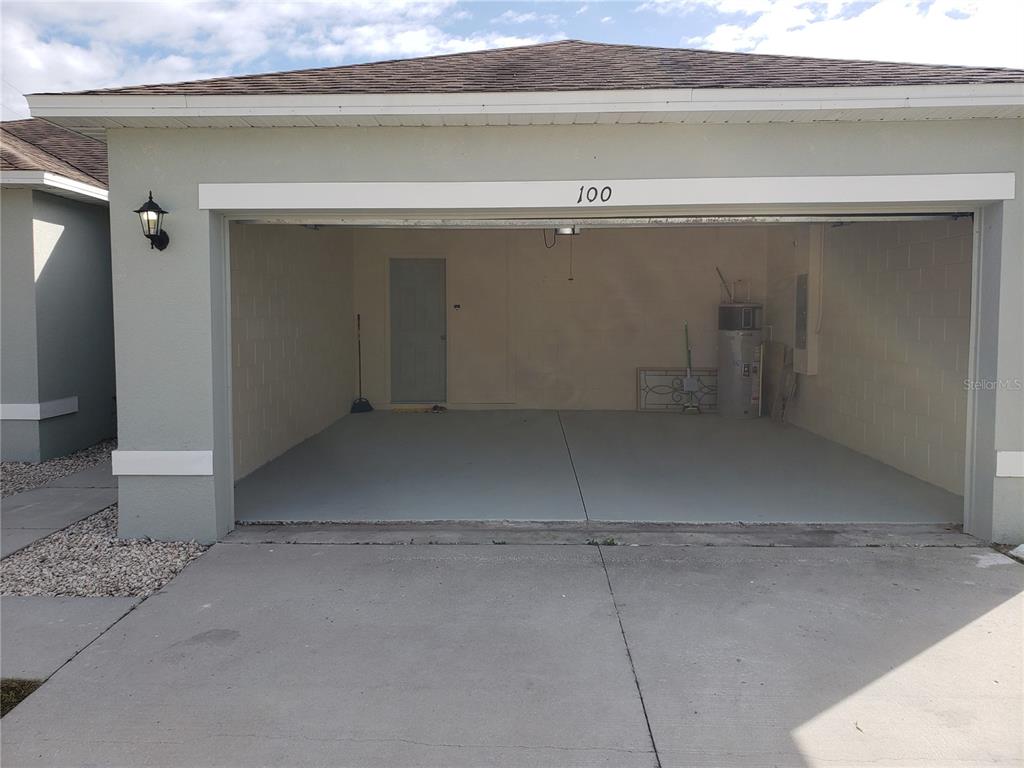 An open two-car garage with a concrete floor, a water heater, and a side door — 100 SWEET PEA COURT, POINCIANA, FL