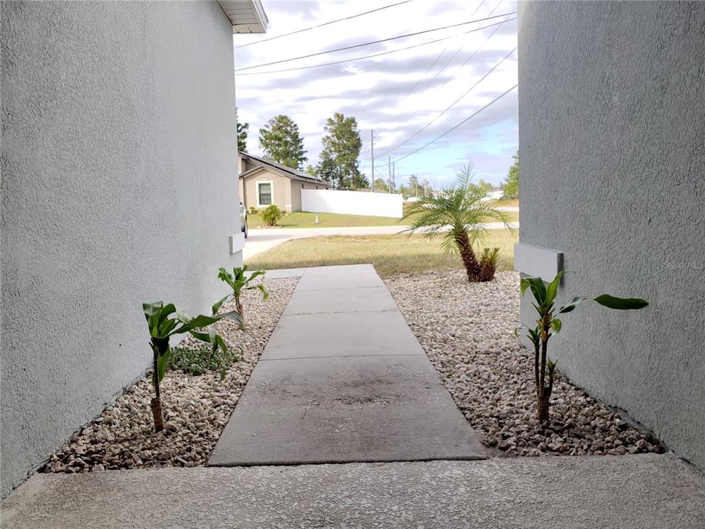 A concrete walkway leads from a covered entryway toward a suburban street and house — 100 SWEET PEA COURT, POINCIANA, FL