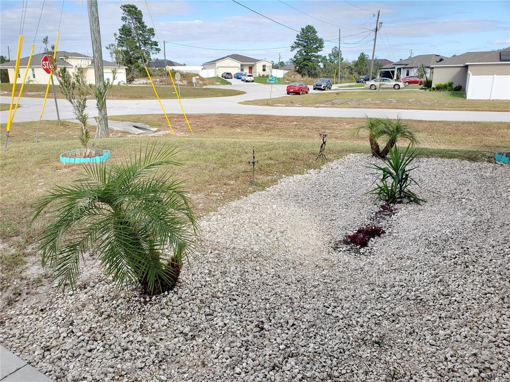 A front yard features a gravel garden bed with small palm trees and shrubs — 100 SWEET PEA COURT, POINCIANA, FL