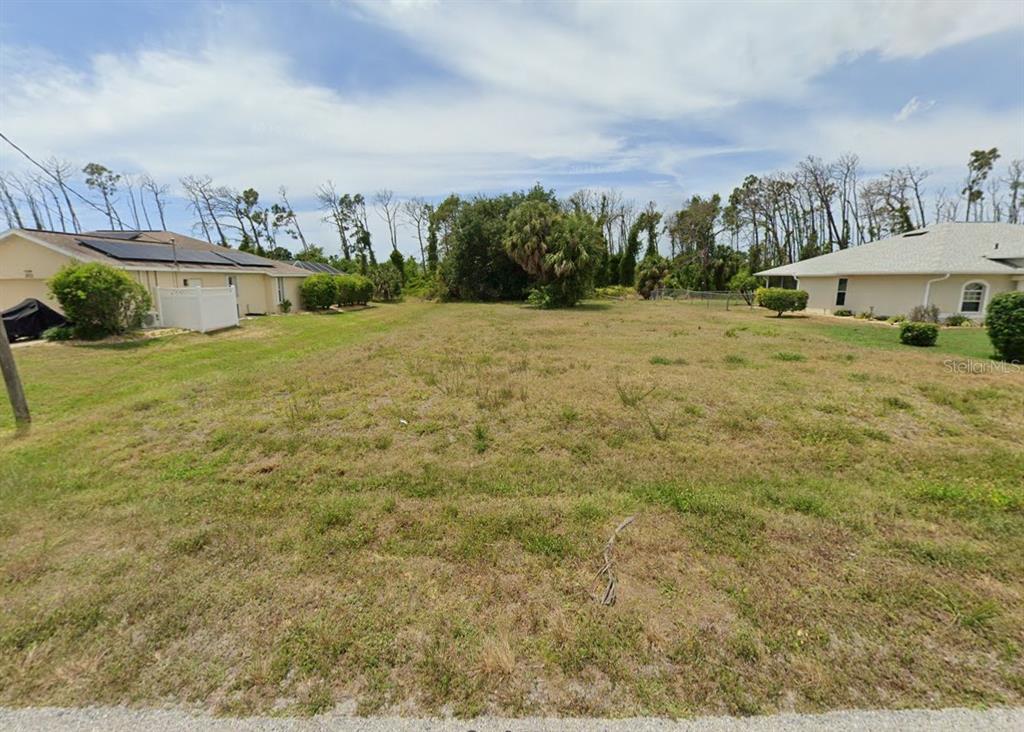 A vacant, grassy residential lot sits between two single-story houses under a cloudy sky — 204 FAIRWAY ROAD, ROTONDA WEST, FL