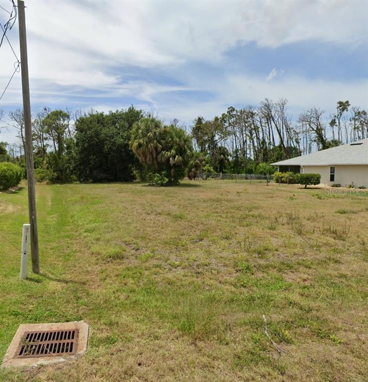 A vacant, grassy residential lot features a storm drain, utility pole, and nearby house — 204 FAIRWAY ROAD, ROTONDA WEST, FL