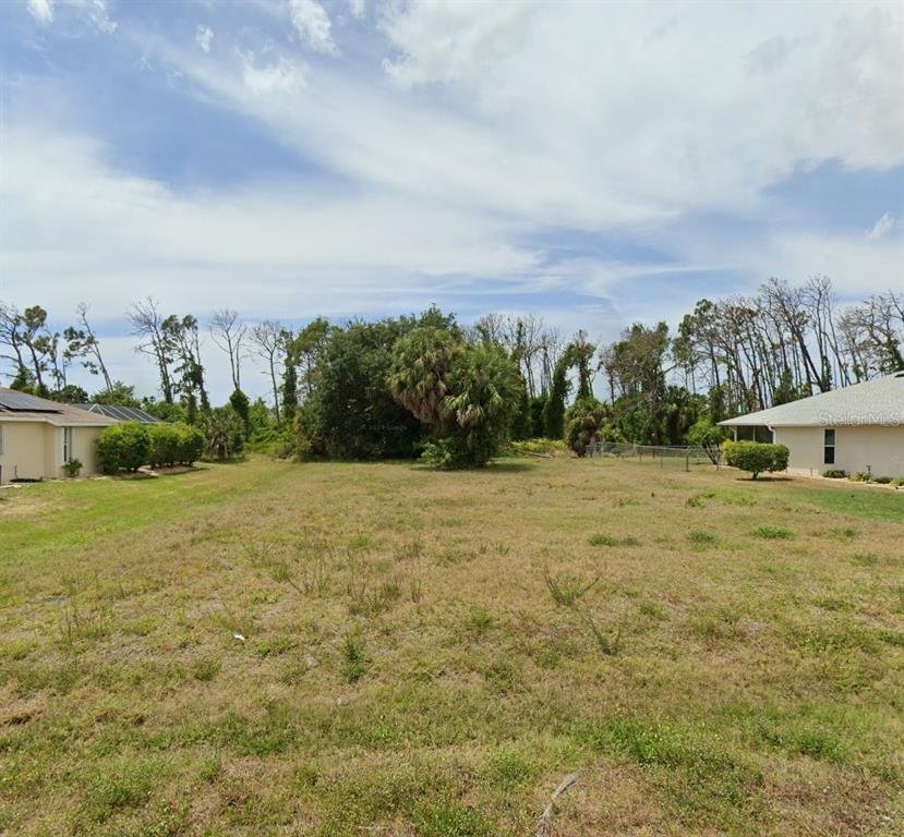 A vacant, grassy residential lot sits between two existing houses under a cloudy sky — 204 FAIRWAY ROAD, ROTONDA WEST, FL