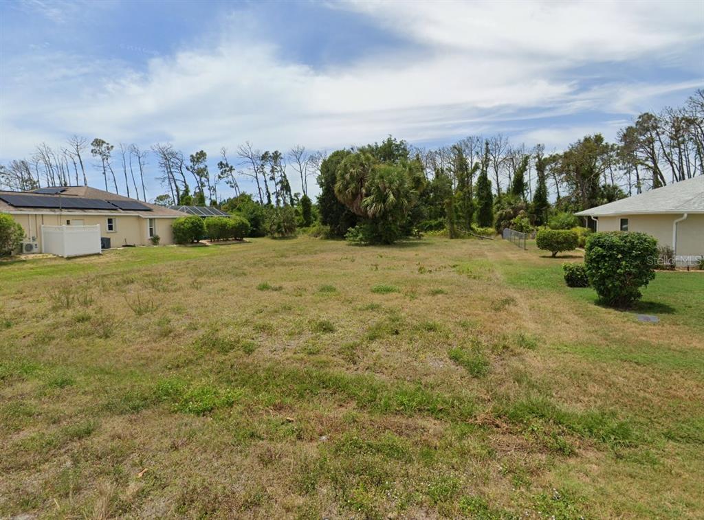 A vacant, grassy residential lot sits between two single-story houses under a cloudy sky — 204 FAIRWAY ROAD, ROTONDA WEST, FL