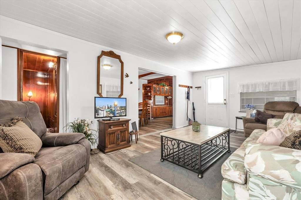A living room features wood-look flooring, a white paneled ceiling, and a view into a kitchen — 1235 MADONA COURT, PUNTA GORDA, FL