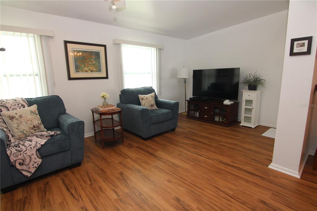A living room features two blue armchairs, a television on a stand, and wood flooring — 810 OAKMONT AVENUE, SUN CITY CENTER, FL