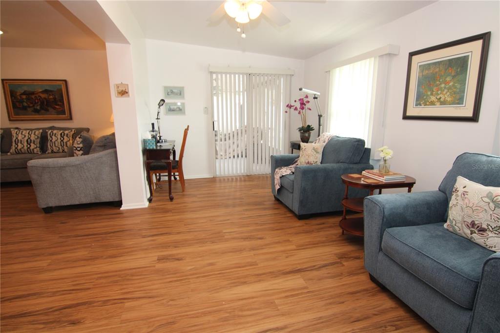 A living room features wood-look flooring, blue armchairs, a small desk, and sliding glass doors — 810 OAKMONT AVENUE, SUN CITY CENTER, FL