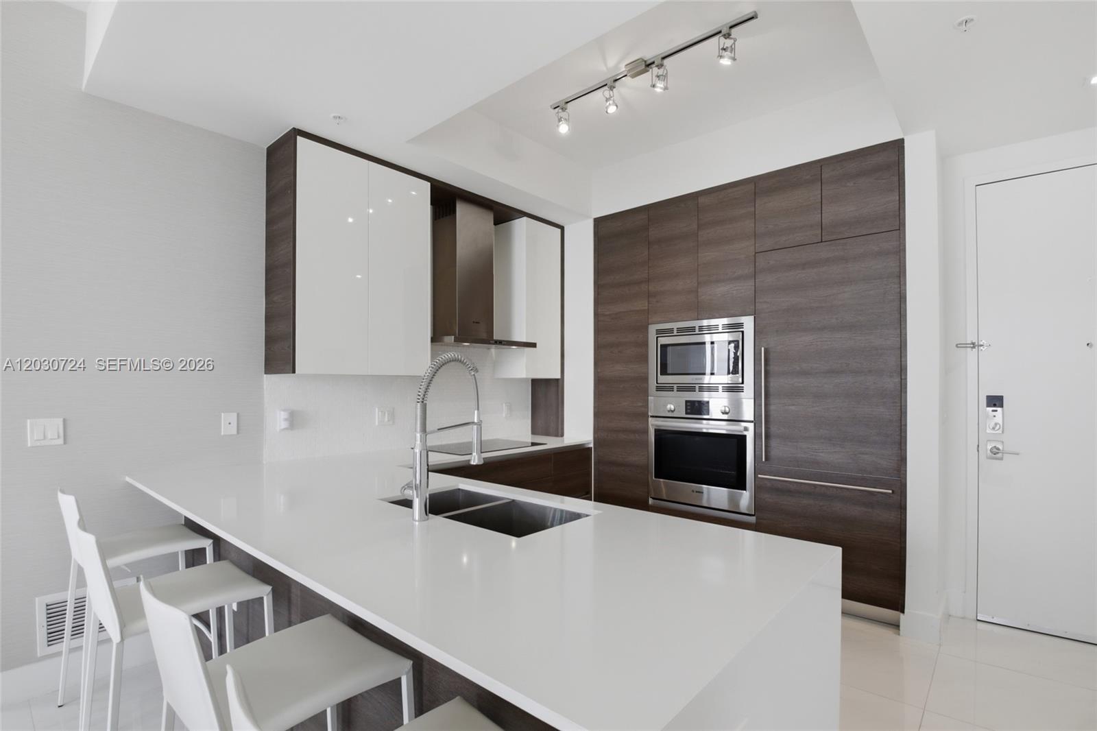 A modern kitchen features white countertops, dark wood cabinetry, stainless steel appliances, and bar seating — 301 Altara Ave, Coral Gables FL 33146, CORAL GABLES, FL