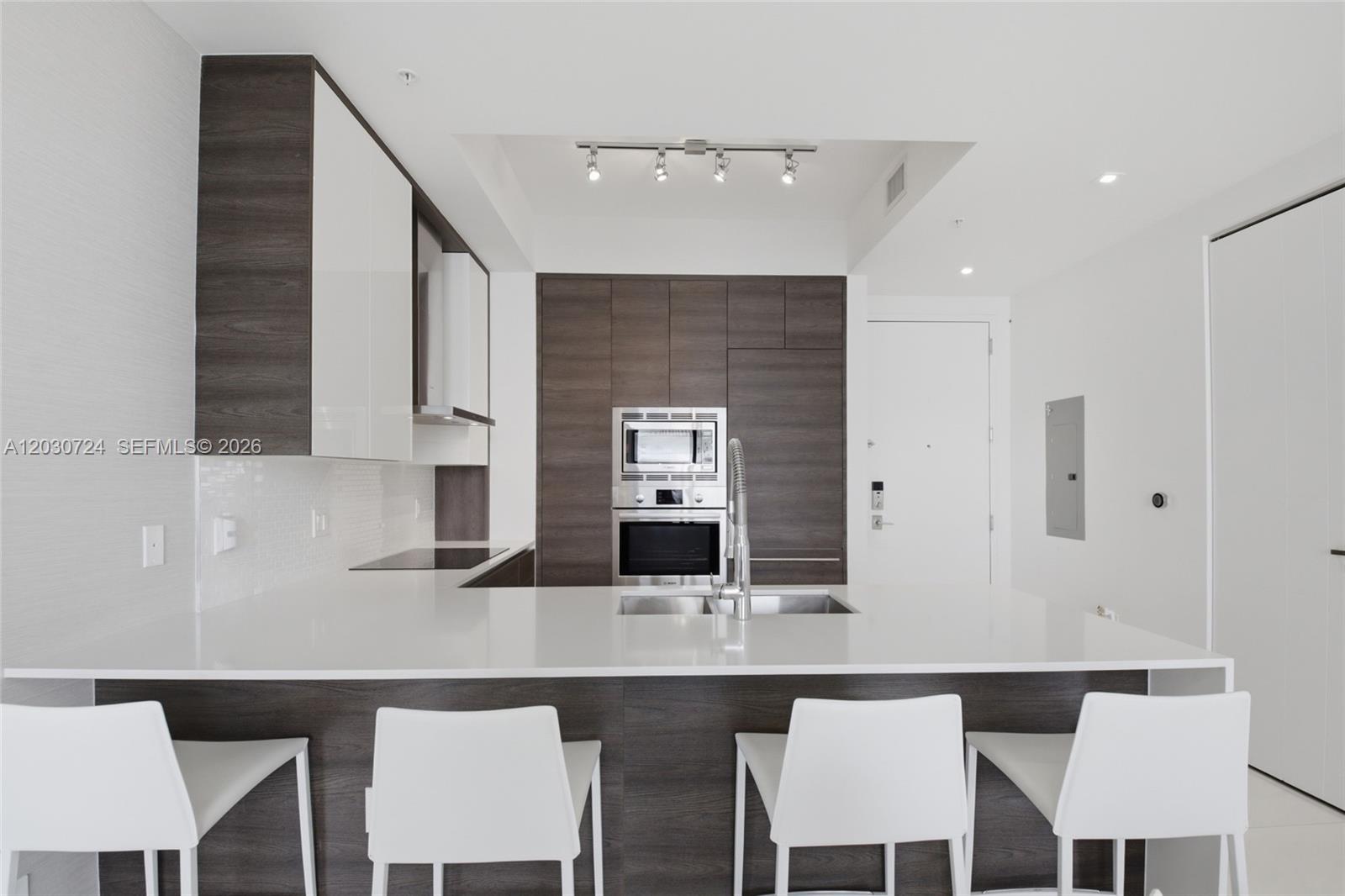 A modern kitchen features dark wood cabinetry, white countertops, a central island, and four chairs — 301 Altara Ave, Coral Gables FL 33146, CORAL GABLES, FL