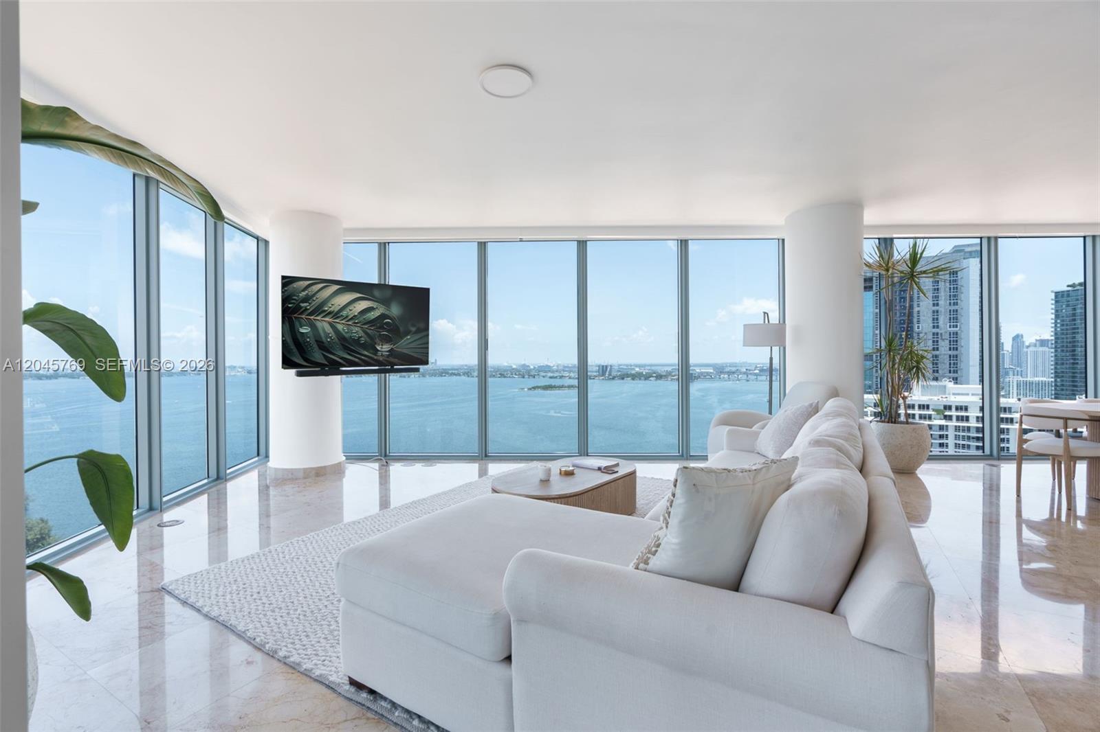 A living room features floor-to-ceiling windows with water views, a white sectional, and marble floors — 601 NE 36th St # 3112, Miami FL 33137, MIAMI, FL