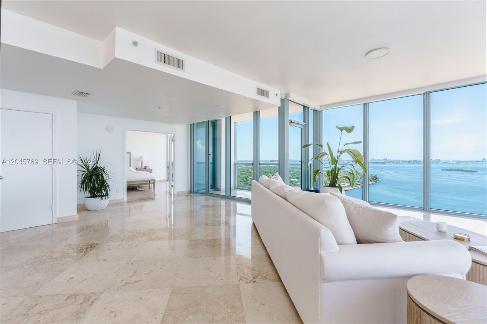 A bright living room features marble floors, a white sofa, and floor-to-ceiling windows overlooking water — 601 NE 36th St # 3112, Miami FL 33137, MIAMI, FL