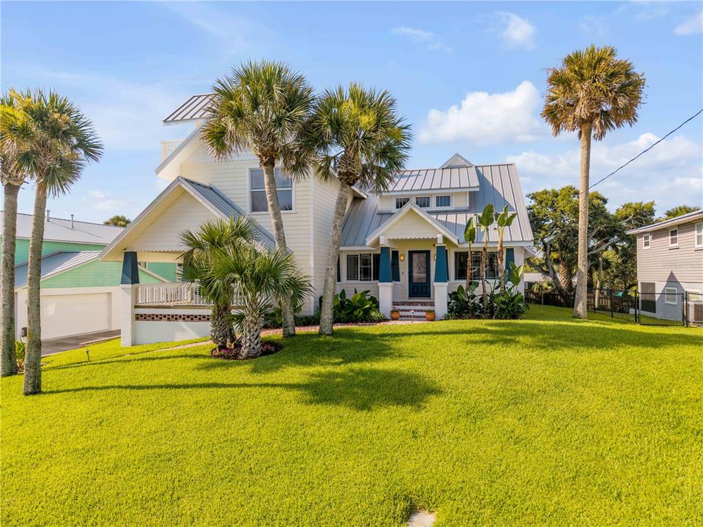 A two-story yellow house with a metal roof and palm trees on a grassy lawn — 315 DUE EAST STREET, NEW SMYRNA BEACH, FL