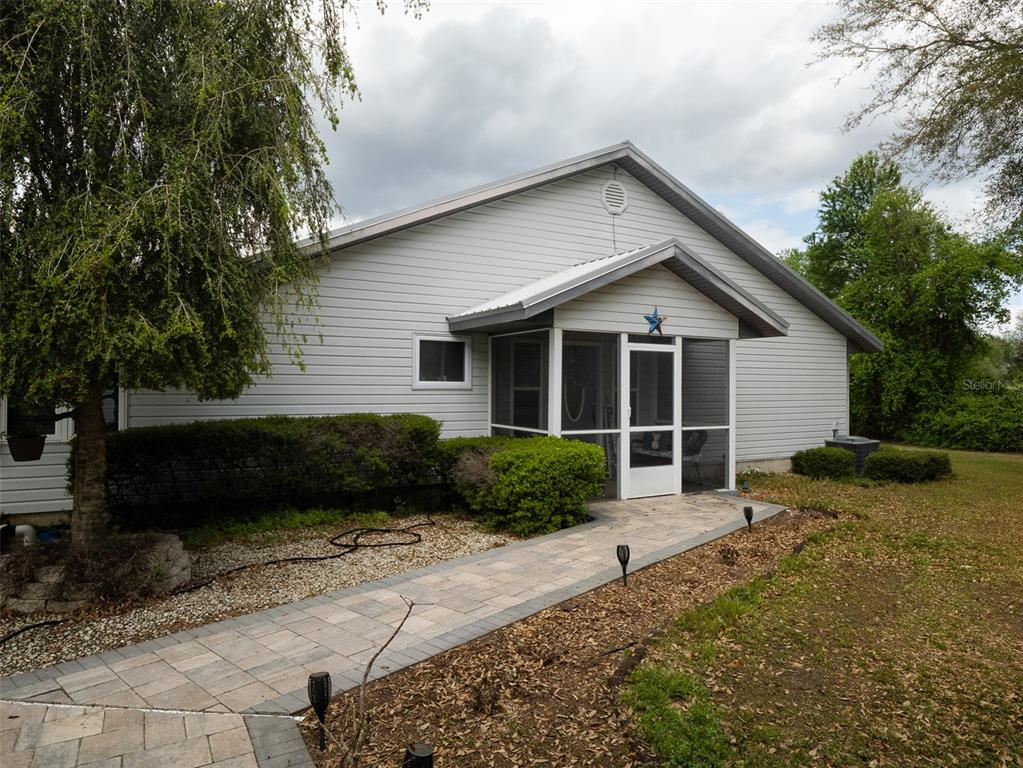 A light-gray vinyl-sided house features a screened-in front porch and a paved stone walkway — 5119 HESKETT LANE, KEYSTONE HEIGHTS, FL