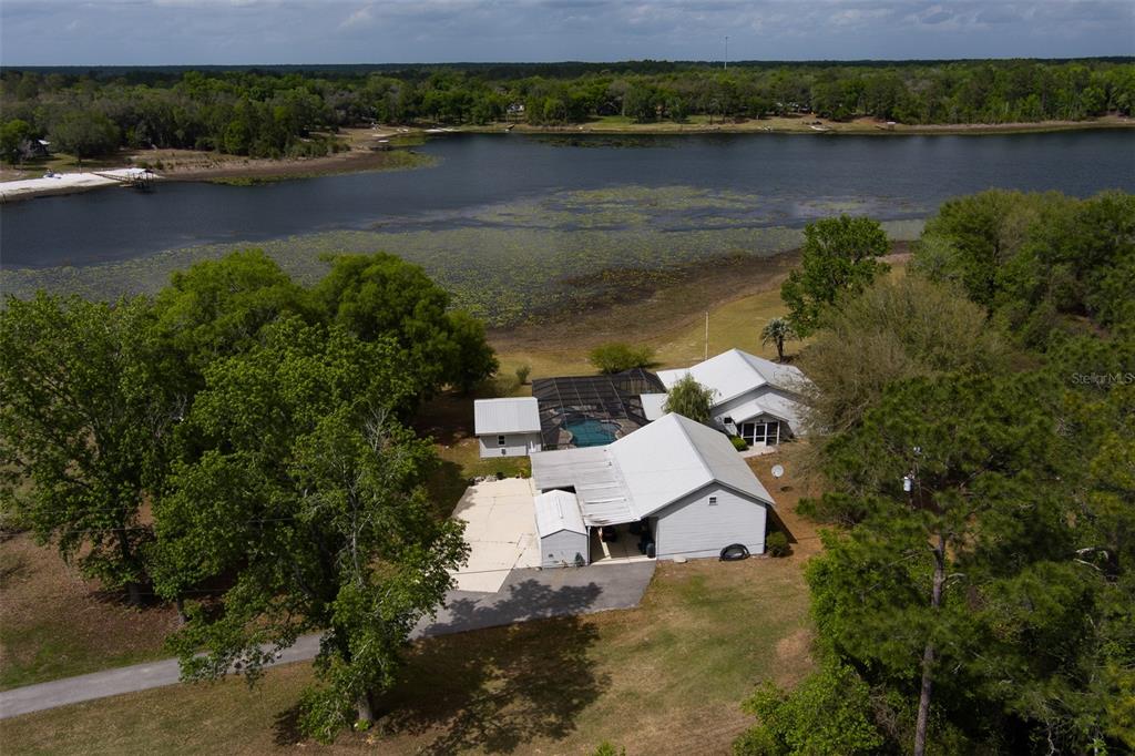 An aerial view shows a house with a pool enclosure situated beside a large lake — 5119 HESKETT LANE, KEYSTONE HEIGHTS, FL