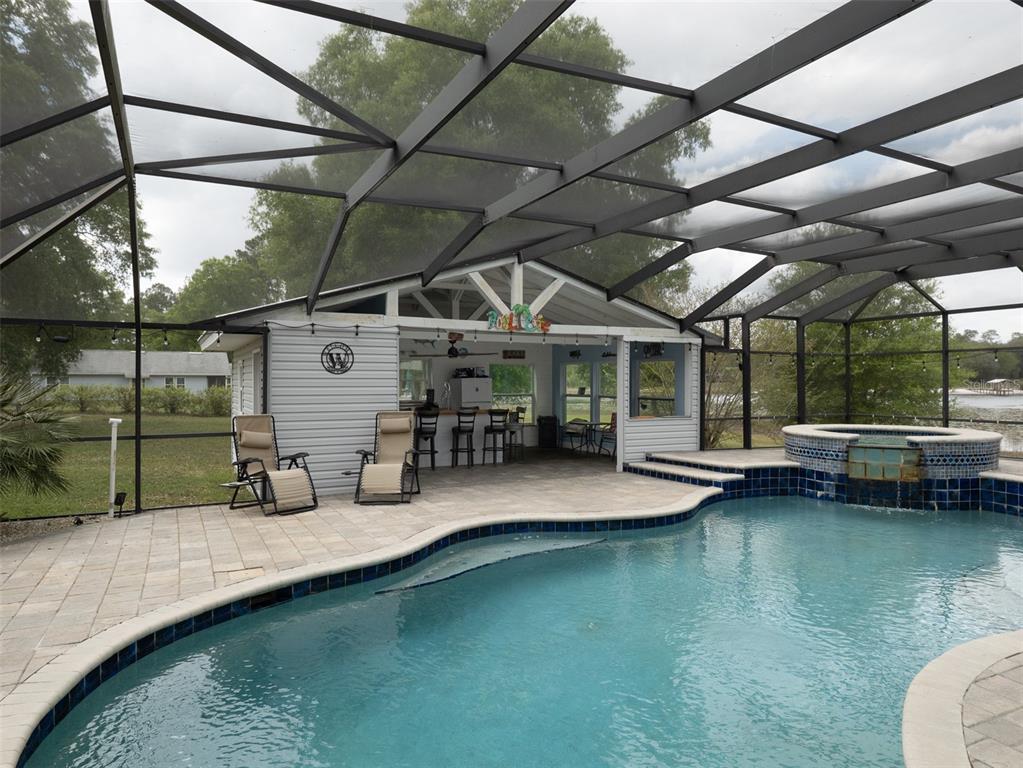 A screened-in pool area features a patio, a swimming pool, a hot tub, and a bar — 5119 HESKETT LANE, KEYSTONE HEIGHTS, FL