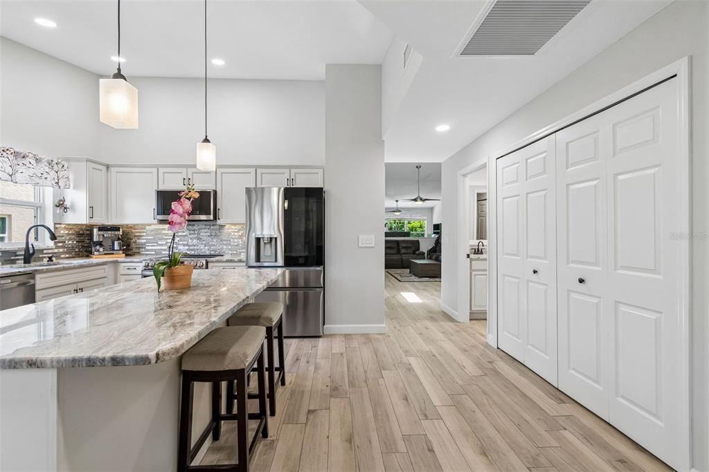 A modern kitchen features white cabinetry, a marble-topped island with two stools, and stainless appliances — 5613 MONTE ROSSO ROAD, SARASOTA, FL