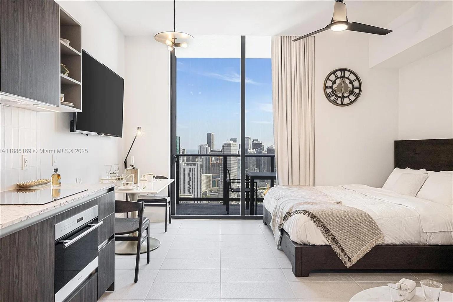 A studio apartment features a kitchenette, a bed, and a balcony with city skyline views — 159 NE 6th St # 5106, Miami FL 33132, MIAMI, FL