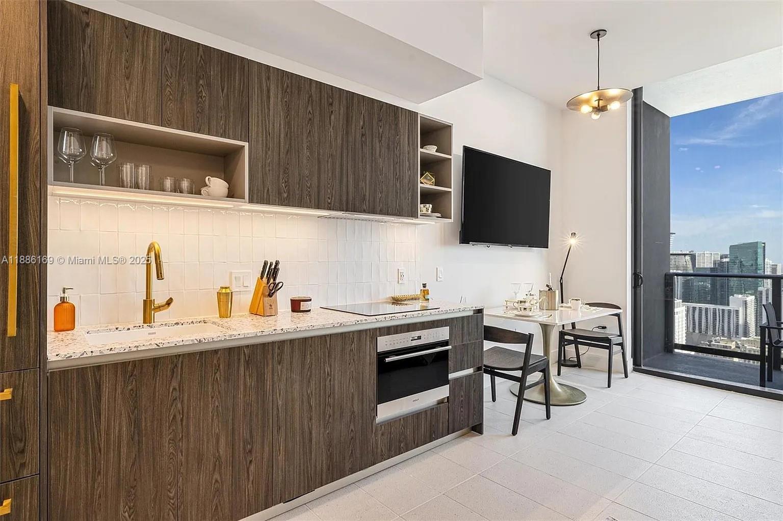 A modern kitchen features wood-grain cabinets, white tile backsplash, and a dining area with balcony — 159 NE 6th St # 5106, Miami FL 33132, MIAMI, FL
