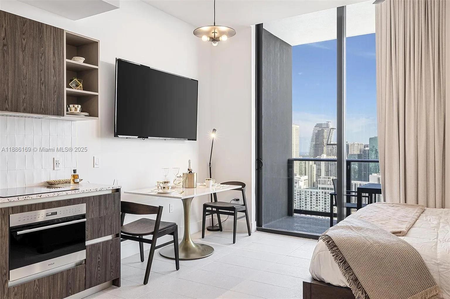A studio apartment features a kitchenette, dining area, and balcony overlooking a city skyline — 159 NE 6th St # 5106, Miami FL 33132, MIAMI, FL